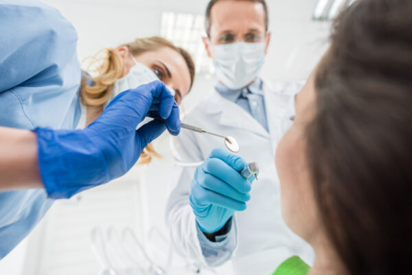 Doctors checking patient teeth with mirror in modern dental clinic